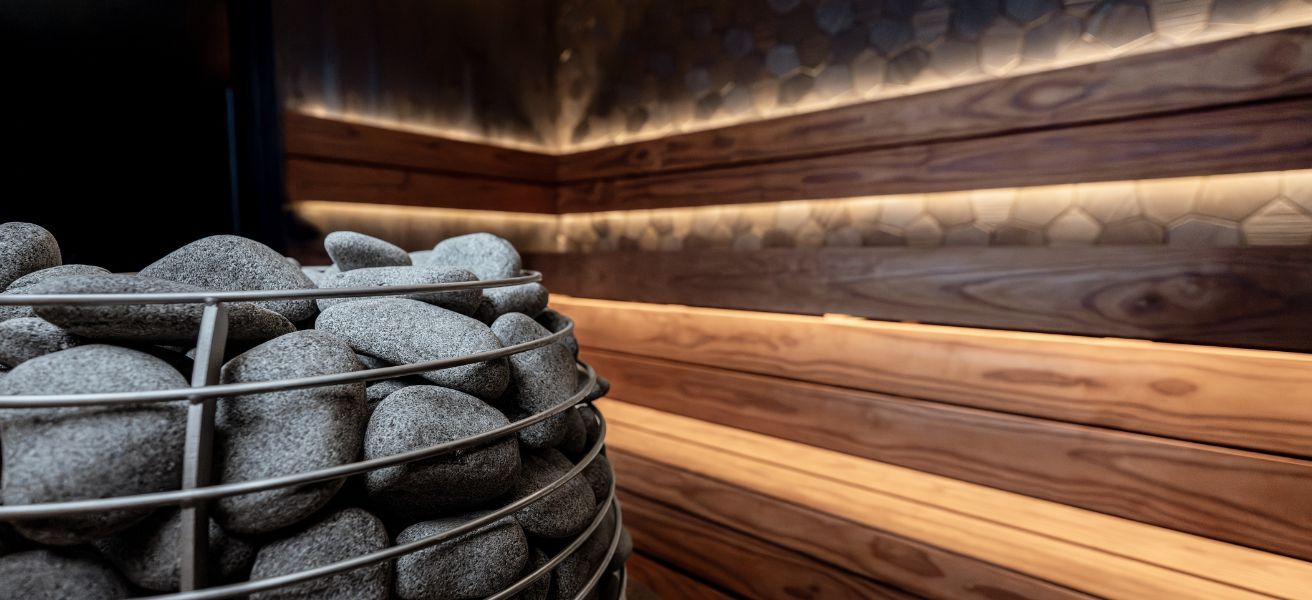 Nowoczesny piec elektryczny do sauny wypełniony kamieniami na tle podświetlanych ław drewnianych – analiza kosztów energii.